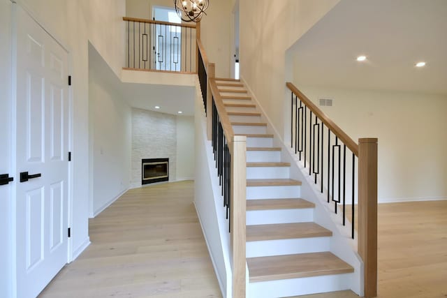 stairs featuring an inviting chandelier, a towering ceiling, a stone fireplace, and hardwood / wood-style floors