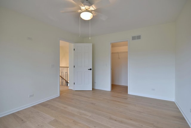 unfurnished bedroom featuring ceiling fan, a walk in closet, light hardwood / wood-style floors, and a closet