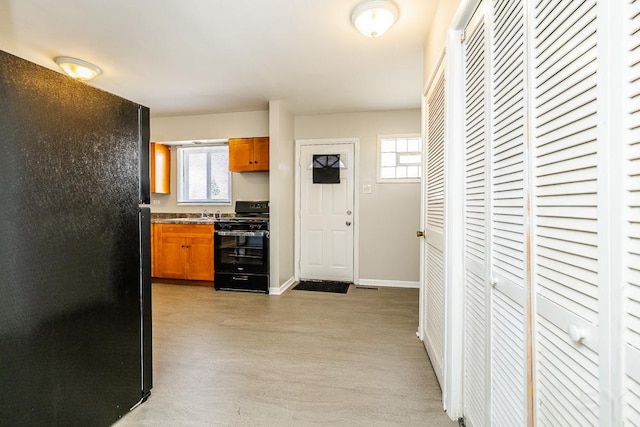 kitchen featuring black appliances, brown cabinetry, light wood-style flooring, and baseboards