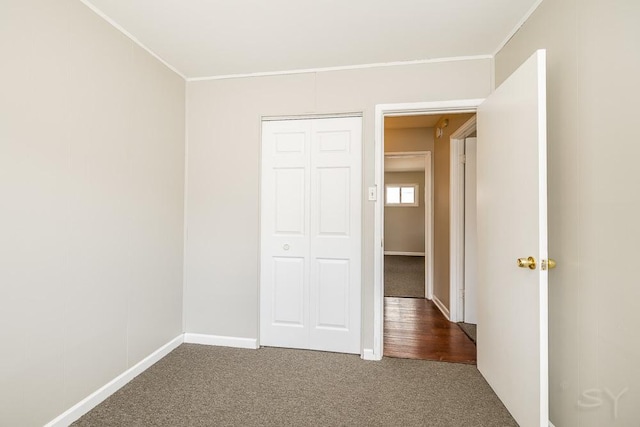 unfurnished bedroom with crown molding, a closet, baseboards, and carpet flooring