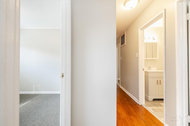 hall with wood finished floors, a sink, visible vents, baseboards, and carpet