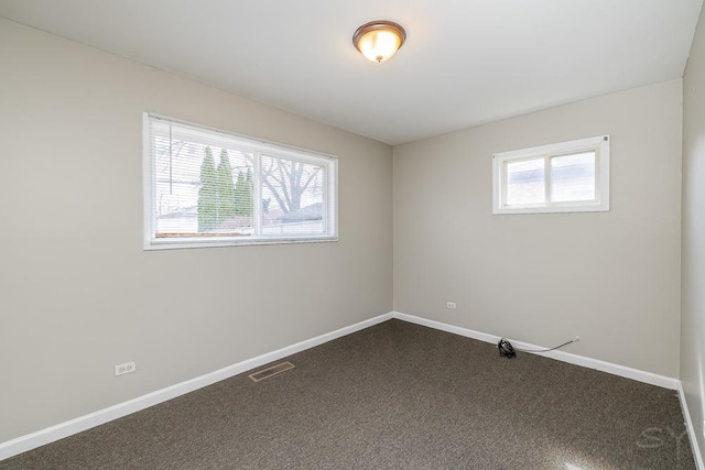 unfurnished room featuring a healthy amount of sunlight, baseboards, visible vents, and dark carpet