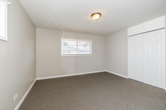 unfurnished bedroom featuring baseboards, dark carpet, and a closet