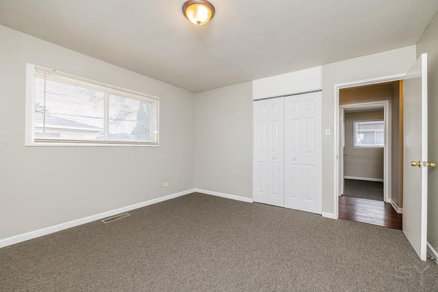 unfurnished bedroom with baseboards, visible vents, dark colored carpet, and a closet