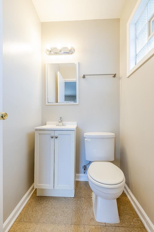 half bathroom featuring tile patterned floors, vanity, toilet, and baseboards