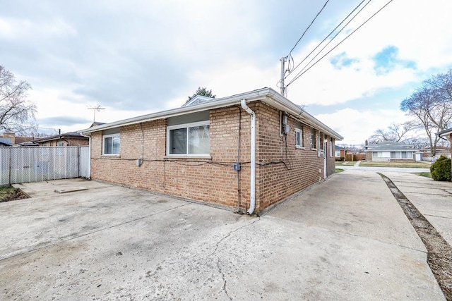 view of side of home with driveway, brick siding, and fence