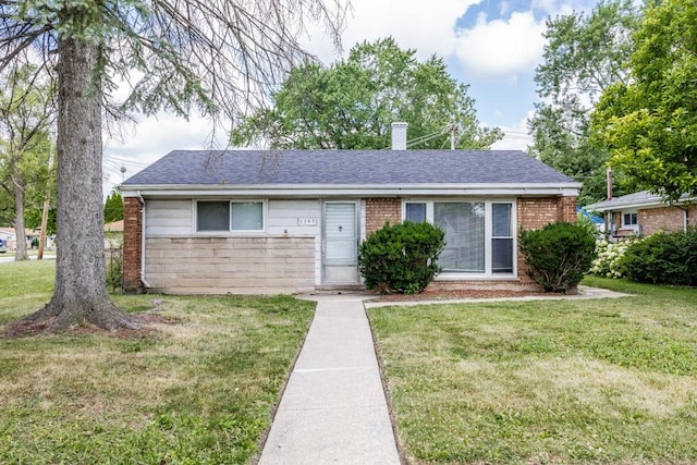 ranch-style home featuring a shingled roof, a front yard, brick siding, and a chimney