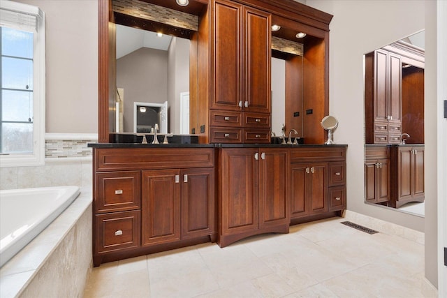 bathroom featuring a relaxing tiled tub, vanity, vaulted ceiling, and a healthy amount of sunlight