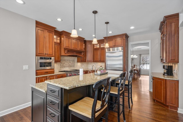 kitchen featuring appliances with stainless steel finishes, a kitchen island, decorative light fixtures, dark hardwood / wood-style flooring, and light stone countertops