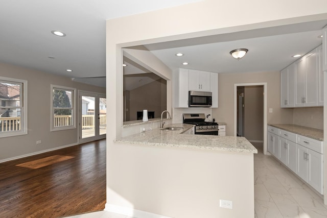 kitchen with light stone counters, a peninsula, a sink, white cabinetry, and appliances with stainless steel finishes