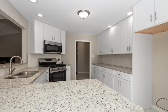 kitchen with appliances with stainless steel finishes, a sink, light stone counters, and white cabinets