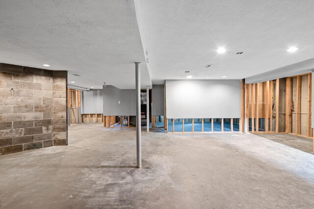 below grade area with a textured ceiling, concrete block wall, and recessed lighting