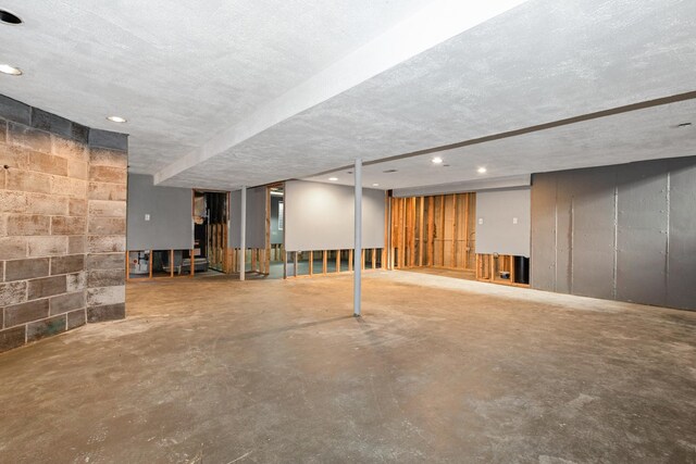 finished below grade area with concrete block wall, a textured ceiling, and recessed lighting