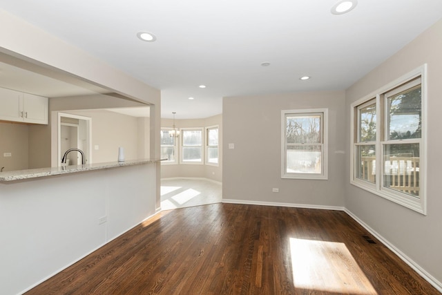 unfurnished living room with dark wood-type flooring, sink, and a notable chandelier