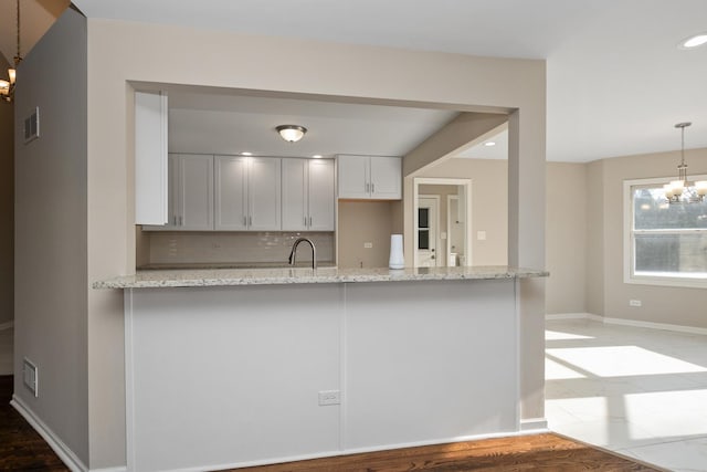 kitchen featuring white cabinetry, decorative light fixtures, light stone countertops, and an inviting chandelier