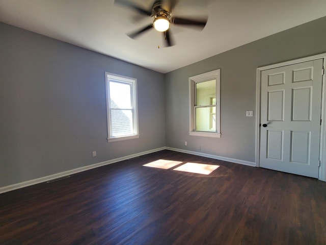 spare room featuring visible vents, baseboards, ceiling fan, and dark wood-type flooring