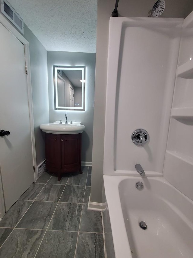 bathroom featuring a textured ceiling, vanity, visible vents, baseboards, and washtub / shower combination