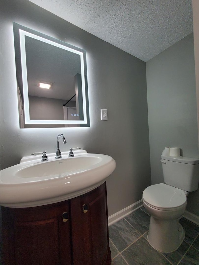 bathroom with a textured ceiling, vanity, toilet, and baseboards