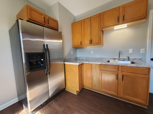 kitchen with brown cabinets, dark wood-type flooring, a sink, light stone countertops, and stainless steel fridge with ice dispenser