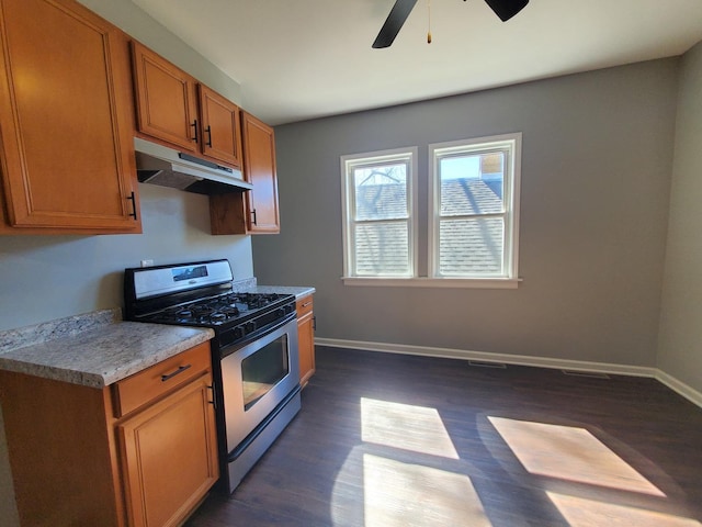 kitchen featuring under cabinet range hood, stainless steel range with gas cooktop, baseboards, and brown cabinetry