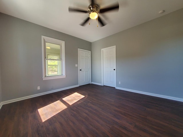 spare room with dark wood-type flooring, a ceiling fan, and baseboards