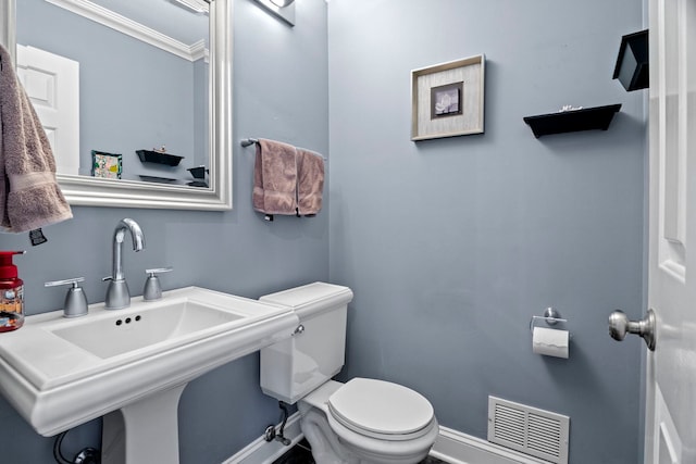 half bathroom with toilet, a sink, visible vents, baseboards, and crown molding