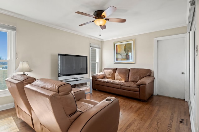 living room with a ceiling fan, visible vents, wood finished floors, and ornamental molding