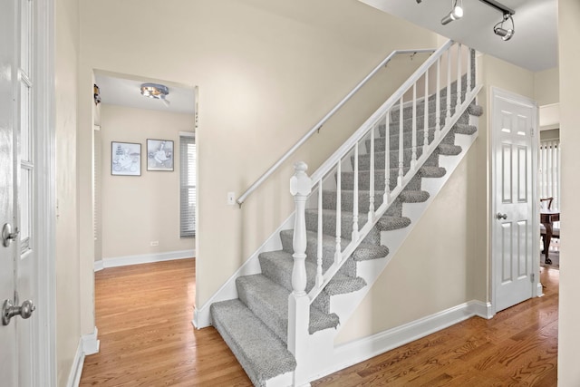 staircase with rail lighting, baseboards, and wood finished floors