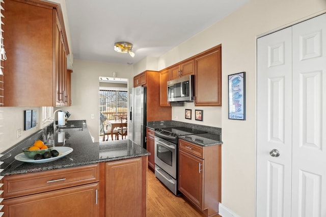 kitchen featuring appliances with stainless steel finishes, dark stone countertops, a sink, and brown cabinets