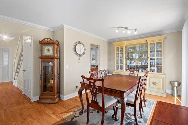 dining area featuring stairs, crown molding, baseboards, and light wood-style floors