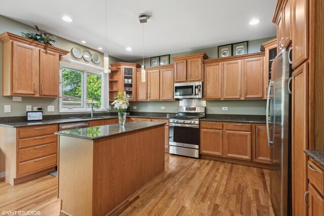 kitchen with dark stone countertops, light hardwood / wood-style floors, a kitchen island, a brick fireplace, and decorative light fixtures