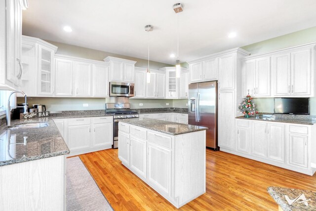 kitchen with appliances with stainless steel finishes, dark stone countertops, hanging light fixtures, a center island, and light wood-type flooring