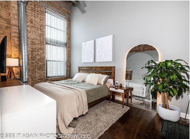 bedroom featuring brick wall, dark wood finished floors, and a high ceiling