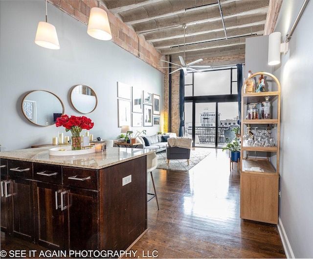 kitchen with a breakfast bar area, dark wood-style flooring, light stone countertops, a high ceiling, and dark brown cabinets