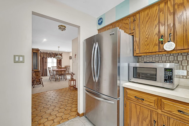 kitchen featuring light colored carpet, appliances with stainless steel finishes, hanging light fixtures, and backsplash