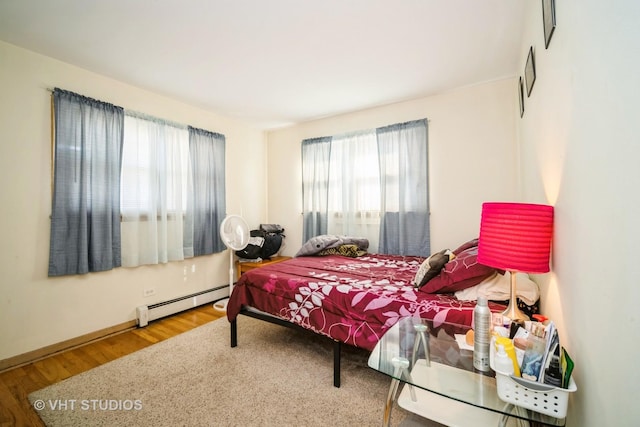 bedroom with wood finished floors, baseboards, and baseboard heating