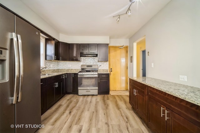 kitchen with under cabinet range hood, light wood-type flooring, light stone counters, decorative backsplash, and stainless steel appliances