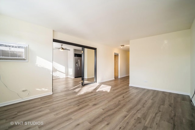 spare room with a ceiling fan, an AC wall unit, wood finished floors, and baseboards