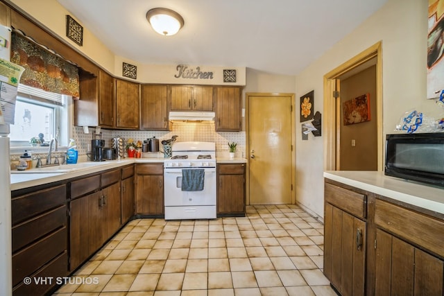 kitchen with white range with gas cooktop, under cabinet range hood, a sink, light countertops, and decorative backsplash