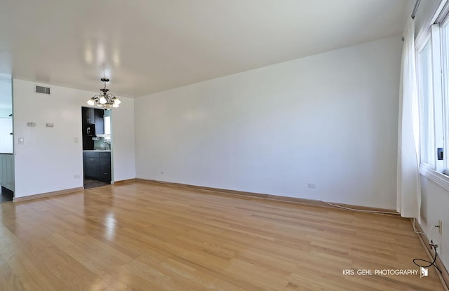 empty room with a notable chandelier, visible vents, light wood-style flooring, and baseboards