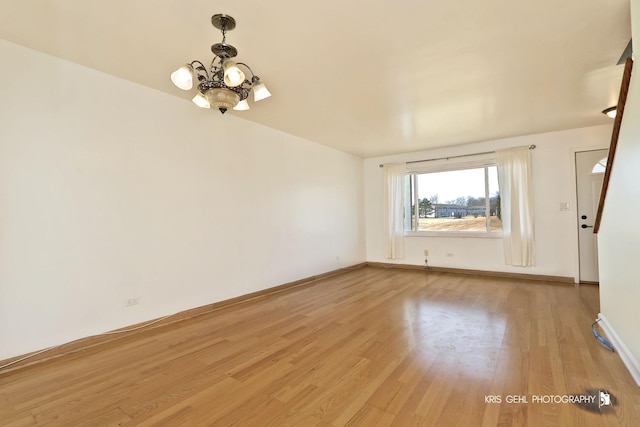 unfurnished room with an inviting chandelier, light wood-style floors, and baseboards