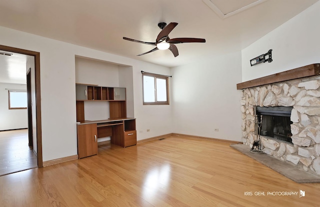 unfurnished living room with a ceiling fan, light wood-style floors, a stone fireplace, baseboards, and built in study area