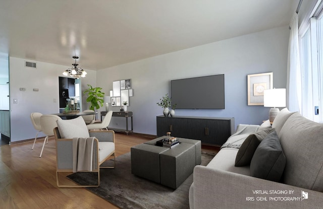 living area with visible vents, baseboards, an inviting chandelier, and wood finished floors