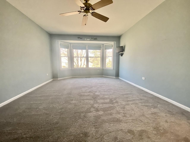 carpeted spare room featuring ceiling fan and baseboards