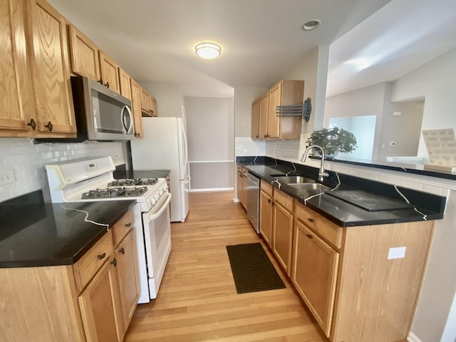 kitchen with dark countertops, light wood-type flooring, a peninsula, stainless steel appliances, and a sink