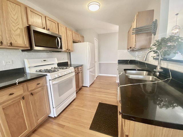 kitchen featuring dark countertops, light brown cabinets, light wood-style floors, white appliances, and a sink