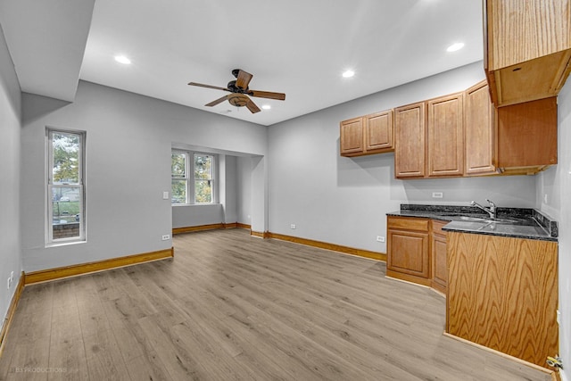 kitchen with ceiling fan, sink, dark stone countertops, and light hardwood / wood-style floors