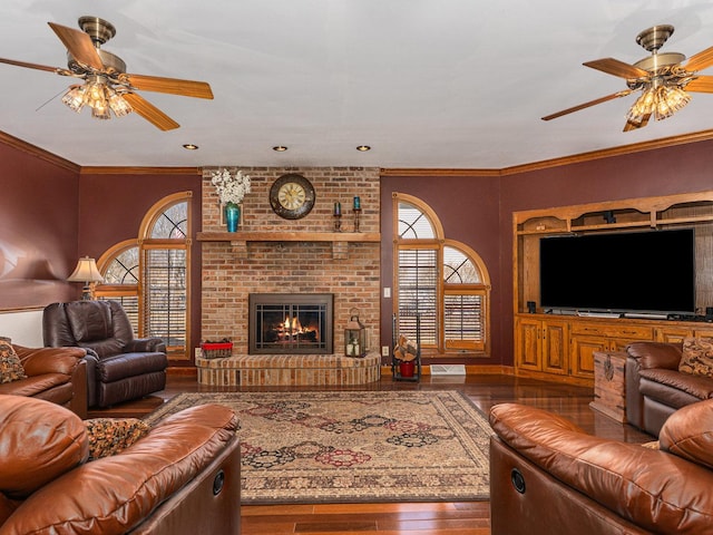 living area with ceiling fan, a brick fireplace, wood finished floors, and crown molding