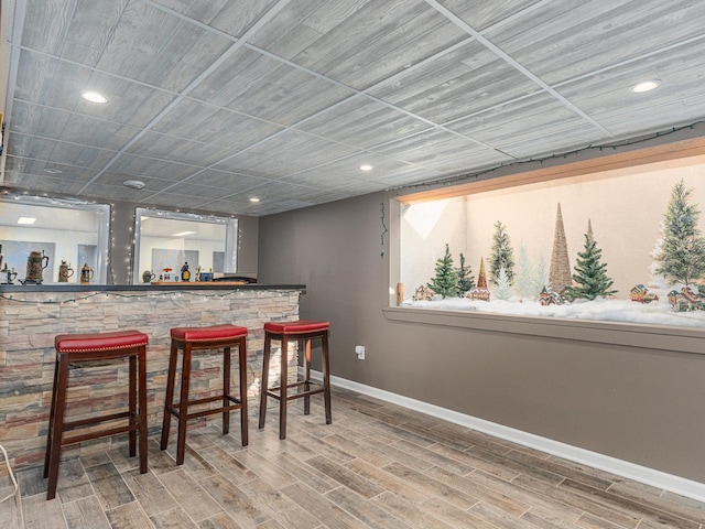 bar with a bar, baseboards, wood finished floors, and recessed lighting