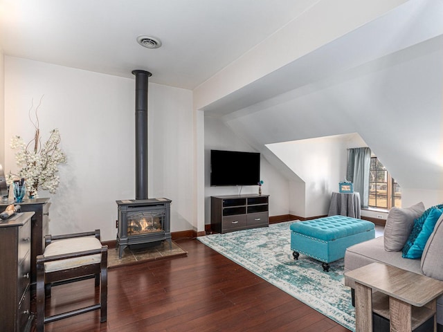 living room featuring baseboards, visible vents, hardwood / wood-style flooring, a wood stove, and vaulted ceiling